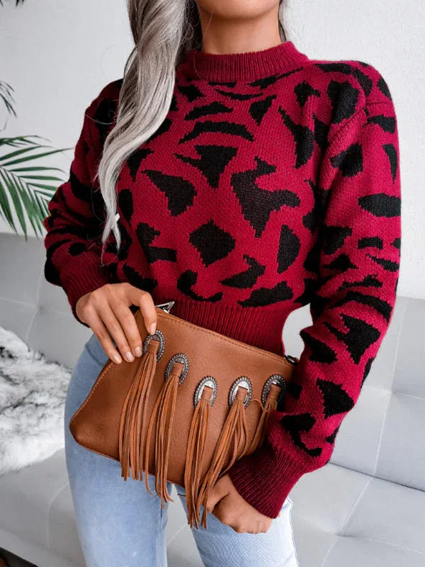 Close-up of a woman in a red and black leopard print cropped knit sweater and light wash jeans, holding a brown fringe clutch.