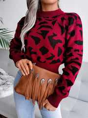 Close-up of a woman in a red and black leopard print cropped knit sweater and light wash jeans, holding a brown fringe clutch.