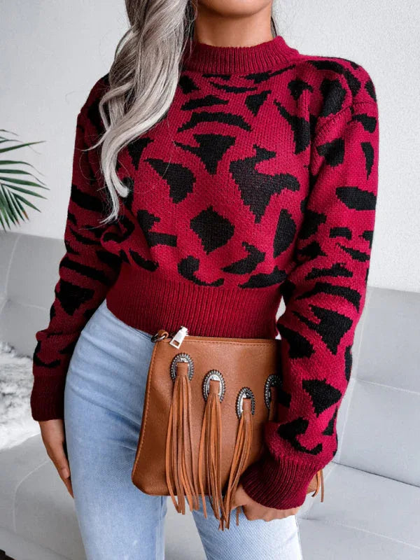 Woman in a red and black leopard print cropped knit sweater, light wash jeans, and a brown fringe clutch, holding the clutch in front of her.
