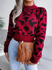 Woman in a red and black leopard print cropped knit sweater, light wash jeans, and a brown fringe clutch, holding the clutch in front of her.