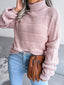 Woman wearing a pink knit turtleneck sweater with light blue jeans and a brown clutch bag.