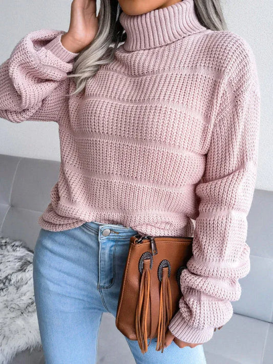 Woman wearing a pink knit turtleneck sweater with light blue jeans and a brown clutch bag.