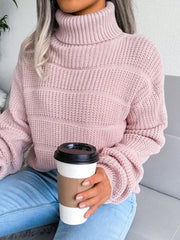 Woman holding a coffee cup while wearing a pink knit turtleneck sweater and light blue jeans.