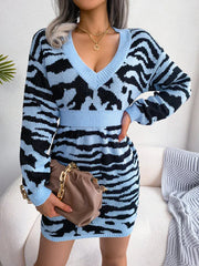 Woman wearing a blue and black tiger print knit mini dress with a V-neck and long sleeves, holding a brown handbag.