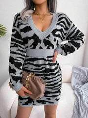 Woman wearing a grey and black tiger print knit mini dress with a V-neck and long sleeves, holding a brown handbag.