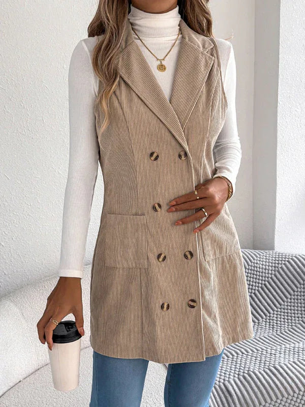Woman wearing a beige corduroy sleeveless blazer over a white turtleneck and blue jeans, holding a coffee cup.