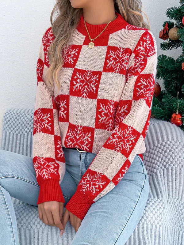 Woman sitting on a couch wearing a red and white checkered snowflake print knit sweater and blue jeans.