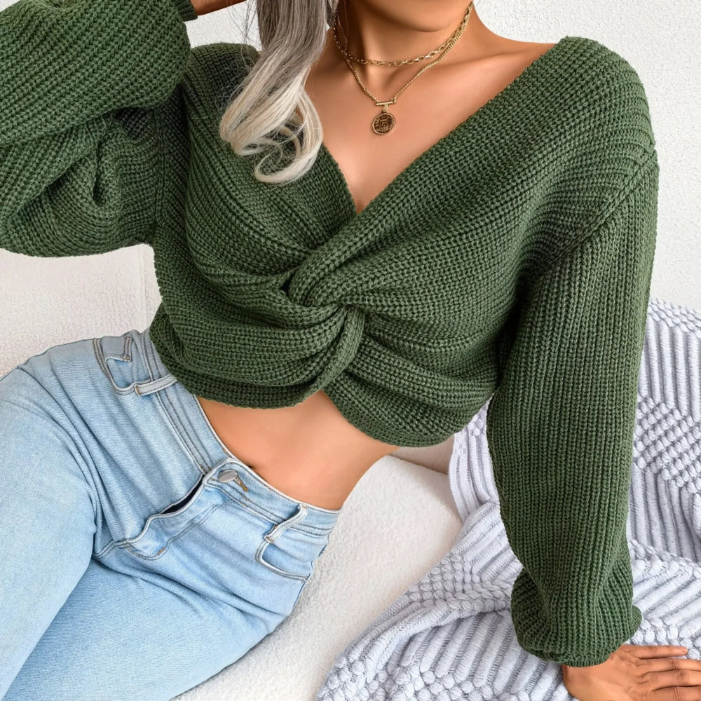 Woman wearing a green ribbed knit cropped sweater with a front twist detail and light wash jeans, sitting on a couch, close-up.