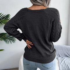 Back view of a woman wearing a charcoal grey cable knit sweater with detailed sleeves, hands on hips.