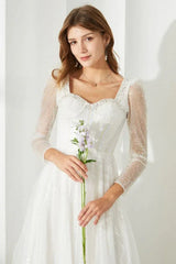 Close-up of a woman holding a flower, wearing a white sequined dress with a square neckline and sheer sleeves.