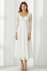 Woman wearing a white sequined A-line dress with sheer long sleeves and a square neckline.