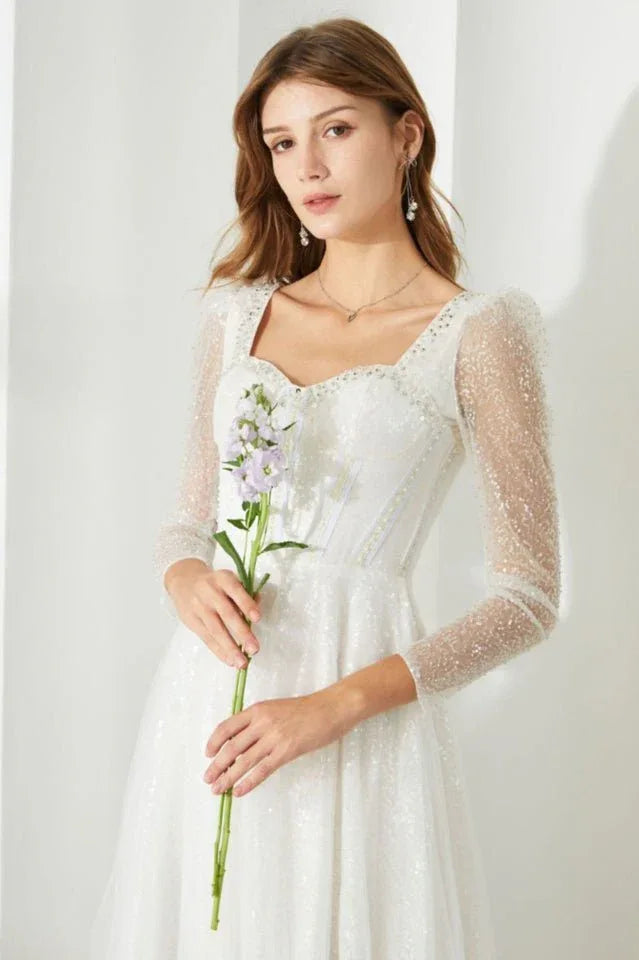 Woman with a bouquet of flowers, showcasing the details of a white sequined dress.