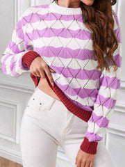 Woman adjusting the hem of a purple and white striped knit sweater with an open-knit geometric pattern, revealing a red underlayer and contrast red cuffs.