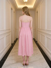Back view of a woman wearing a pink midi dress with spaghetti straps and a square neckline, standing in a hallway.