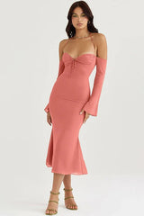 Woman wearing a coral ruched midi dress with detachable sleeves and halter neckline
