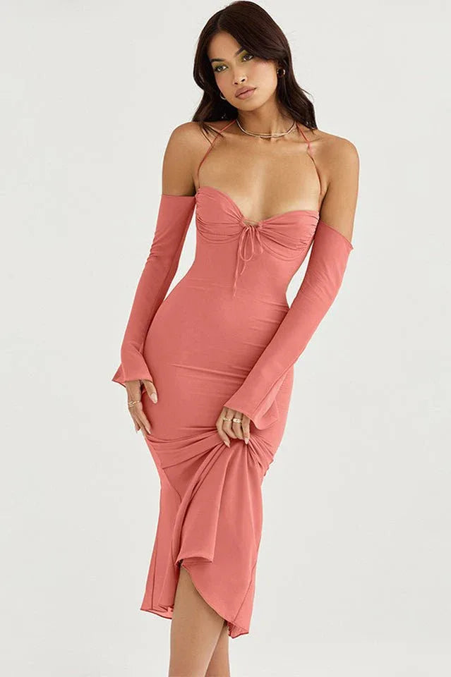 Woman in a coral ruched midi dress with detachable sleeves and halter neckline, holding the hem