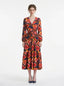 Woman wearing a long-sleeved floral print midi wrap dress with a tiered skirt, standing against a white background.