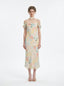 Woman wearing a floral print midi slip dress with off-the-shoulder sleeves and a cowl neckline, standing against a white background.