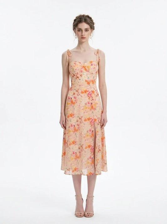 Model wearing a peach floral print midi dress with spaghetti straps and a thigh-high slit, standing against a white background.