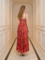 Back view of a woman wearing a red floral print maxi dress with spaghetti straps and a pleated skirt.
