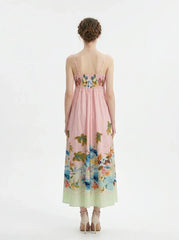Full back view of a woman wearing a pink midi dress with a tropical print and spaghetti straps, standing against a white background.
