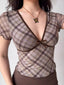 Close-up of a woman wearing a brown and purple plaid v-neck top with a bow detail.