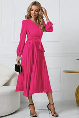 Woman posing in a long-sleeved pink wrap dress with a pleated skirt and a self-tie belt