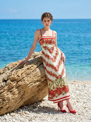 Woman wearing a floral print maxi dress with spaghetti straps, leaning against a large rock on a beach.