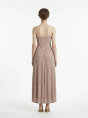 Back view of a woman in a strapless, metallic knit maxi dress with a self-tie belt.