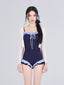Woman wearing a navy one-piece swimsuit with ruffled blue trim and a sheer white cardigan.