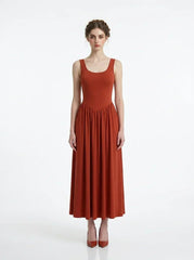 woman wearing a rust-colored ribbed knit midi dress with a scoop neckline and sleeveless design, standing against a white background