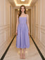 Woman wearing a purple midi dress with spaghetti straps and a square neckline, standing in a hallway.