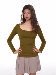 Model wearing a fitted, olive green, long-sleeved, scoop neck top with a ribbed texture and ruched side detail.