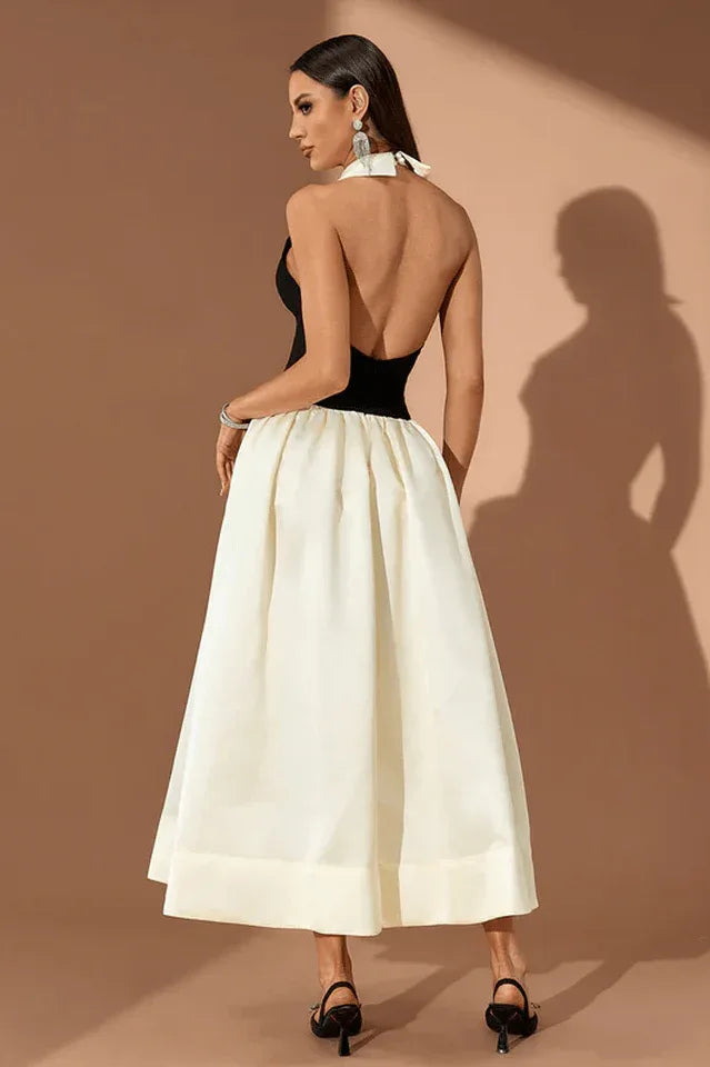 Back view of a woman wearing a black and ivory halter gown with a large collar, standing against a brown background.