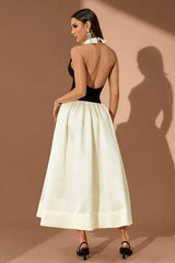 Back view of a woman wearing a black and ivory halter gown with a large collar, standing against a brown background.