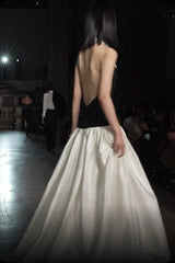 Model on a runway from behind wearing a black and ivory halter gown with a large collar and flowing skirt.