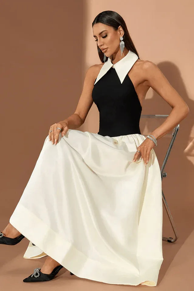 Woman wearing a black and ivory halter gown with a large collar, sitting on a chair against a brown background.