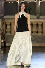 Model on a runway wearing a black and ivory halter gown with a large collar.