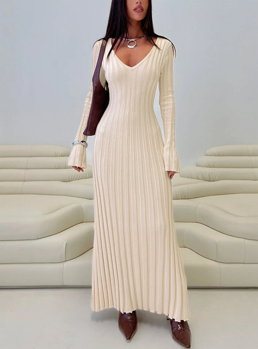 Woman wearing a cream ribbed knit maxi dress with long sleeves and a v-neckline, accessorized with a brown shoulder bag, silver necklace, and silver bracelet.