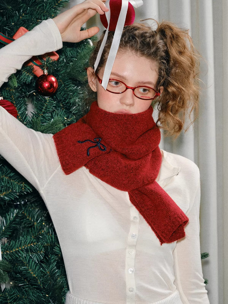Woman adjusting a red knit scarf around her neck, with a Christmas tree to the side.