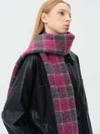 Close-up of a woman wearing a pink and grey plaid scarf around her neck, over a black leather-look jacket.
