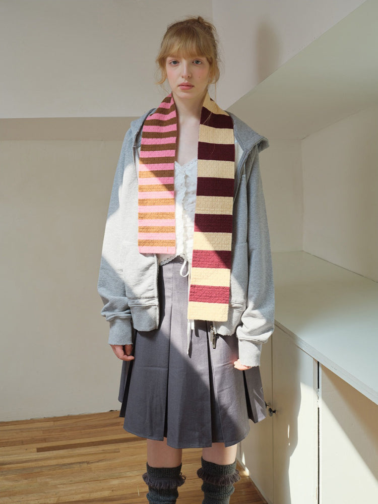 Model wearing a white lace camisole, grey zip-up hoodie, grey pleated skirt, and a striped scarf with pink and brown stripes.