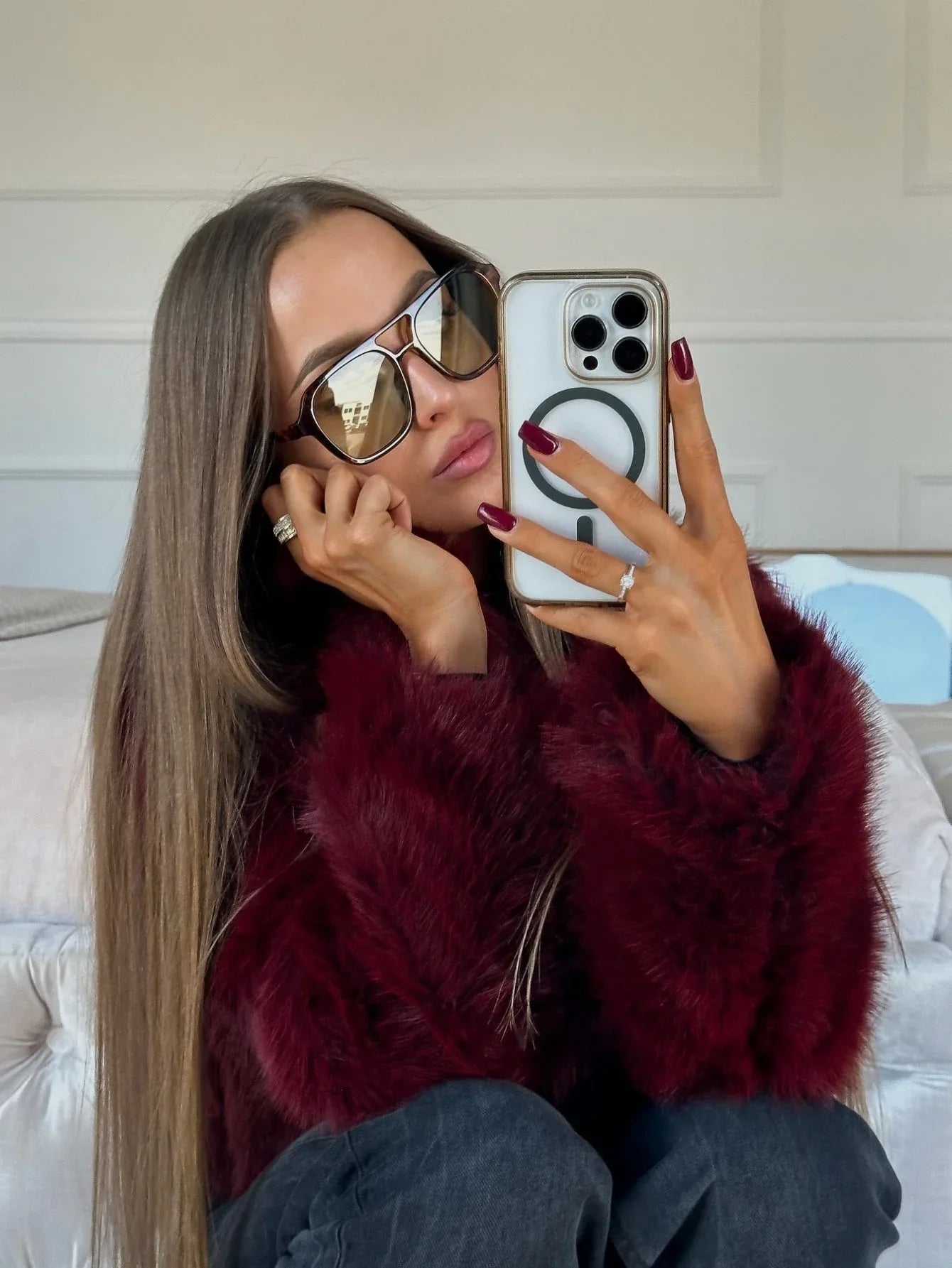 Woman taking a selfie in a mirror wearing a burgundy faux fur jacket and sunglasses