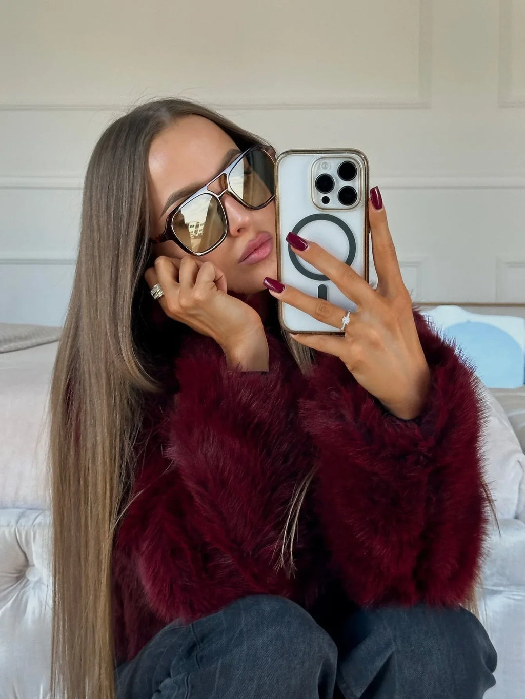 Woman taking a selfie in a mirror wearing a burgundy faux fur jacket and sunglasses
