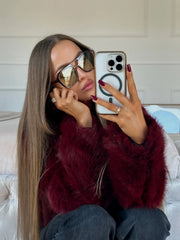 Woman taking a selfie in a mirror wearing a burgundy faux fur jacket and sunglasses