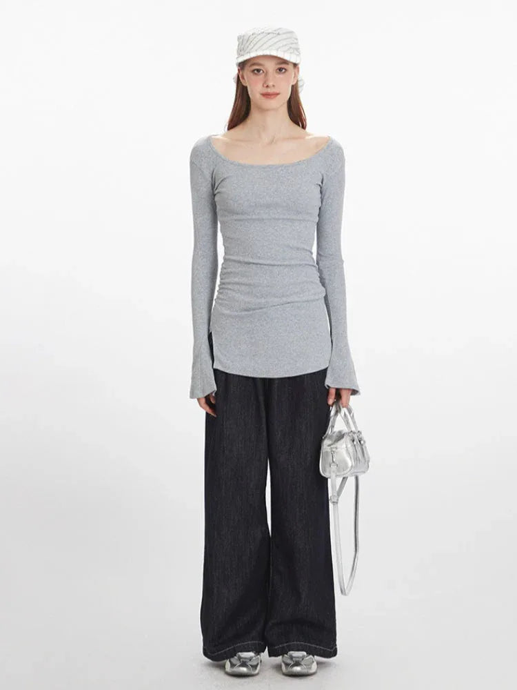 Front view of a woman wearing a grey long-sleeve ribbed knit top with bell sleeves and dark wash wide-leg jeans, holding a silver handbag.