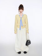 Woman posing with hands in pockets, wearing a yellow knit cardigan and cream wide-leg pants.