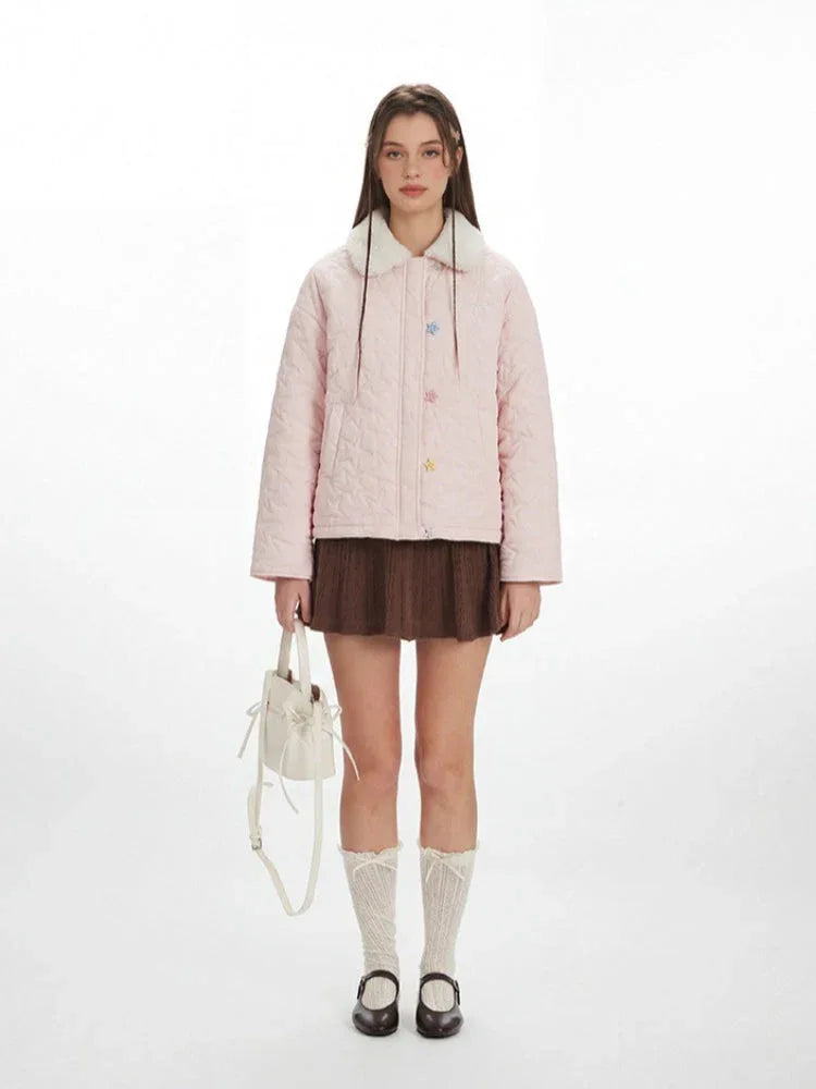 Model wearing a pink quilted jacket with a faux fur collar and star buttons, paired with a brown skirt, white socks, and black shoes.