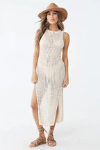 Woman wearing a cream crocheted knit sleeveless maxi dress with a high slit and a wide-brim hat.