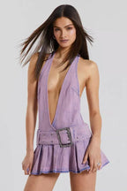Woman wearing a lavender denim halter mini dress with a plunging neckline and a pleated skirt.